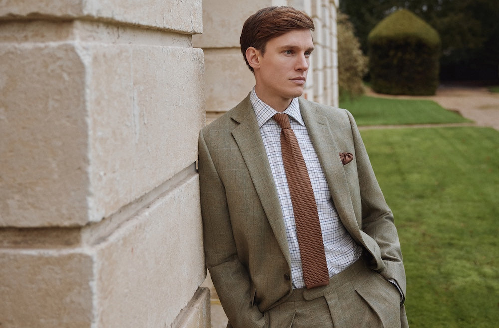 Man sitting down in country home. He wears Oliver Brown; forest green tweed jacket and twill beige trousers.